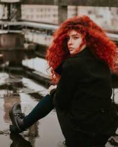 young woman wearing black over coat with long thick wavy red hair 