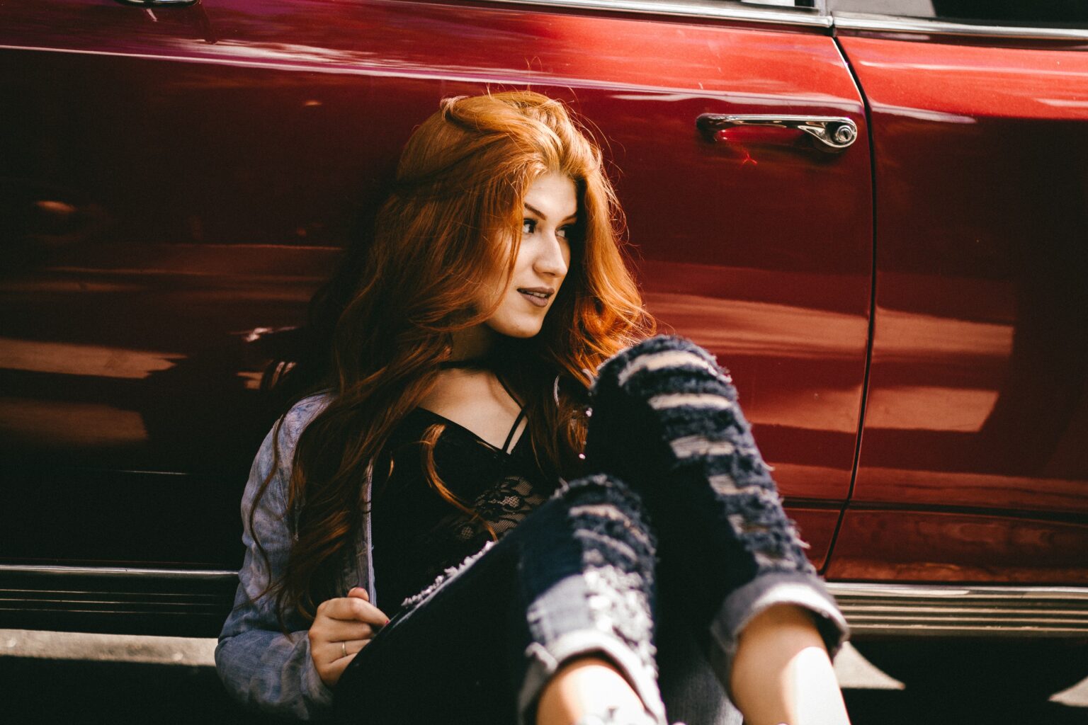BAQ henna powder hair dye on woman sitting against a red car, with long auburn hair colouring