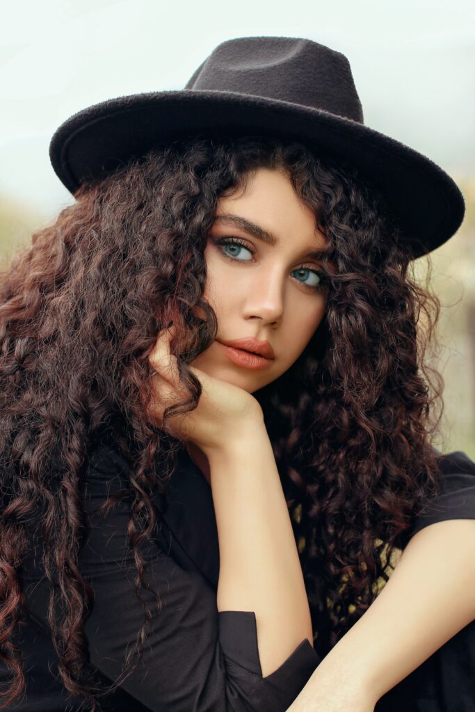 Natural brown hair colouring on beautiful thick long wavy hair on woman dressed in black wearing a black hat