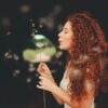 woman with long auburn wavy hair with ppd free auburn henna hair dye, holding a plant and blowing