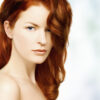 organic henna hair dye on beautiful red head with long wavy hair flowing over one shoulder, wearing a white towel covering upper part of her body