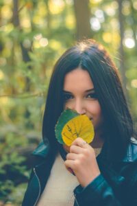 woman with straight short bob dark brown black hair dye holding two leaves up in front of her face