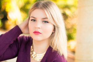  blonde woman with medium length straight hair wearing V neck long sleeve purple top, touching her hair