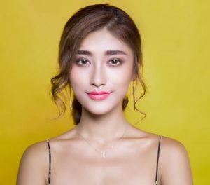 Tumeric Secret Beauty Mix for Glowing Skin, young asian woman with natural looking glowing skin and shiny hair, standing against a full yellow background