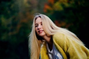 restoring bleached hair is easy with natural hair care products like cassia obovata; woman wearing yellow cardigan leaning forwards with long blonde hair 