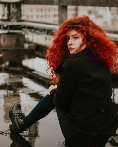 pure henna natural hair dye, red head girl with vibrant thick red wavy curly hair sitting on steps on a rainy day