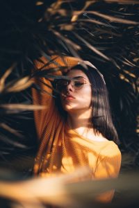 best natural hair dye,, woman in yellow top standing under a tree,touching her long dark brown hair