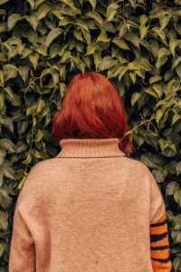 Mixing Henna, Renaissance Henna, photo of back of woman with red hair facing a green bush, wearing a beige jumper