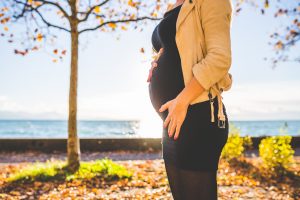 pregnancy and hair dye safety- it's all about making your own informed choice; pregnant mum in black track pants and beige top standing outside in autumn sunshine,and surrounded by autumn leaves on the green grass