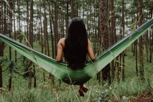 Natural hair dye from plants colours and maintains beautiful hair; woman sitting on a leaf hammock in a forest, with her long black hair down her back