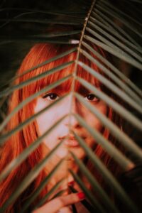 woman with auburn hair with leaf in front of her face