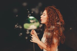 curly haired woman with long henna hair colour holding a plant and blowing