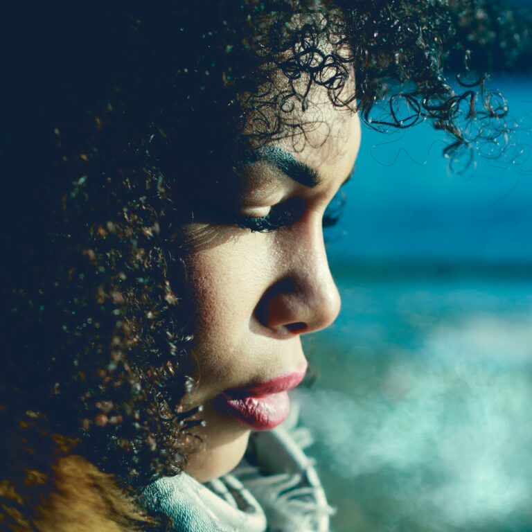 Natural black hair, profile of young black woman with curly black hair against a blue background