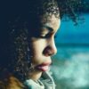 Natural black hair, profile of young black woman with curly black hair against a blue background