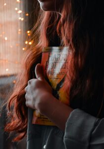 woman with long red hair clasping a Harry Potter book close to her chest, mystical aura, cant see her face just her long hair draping the book 