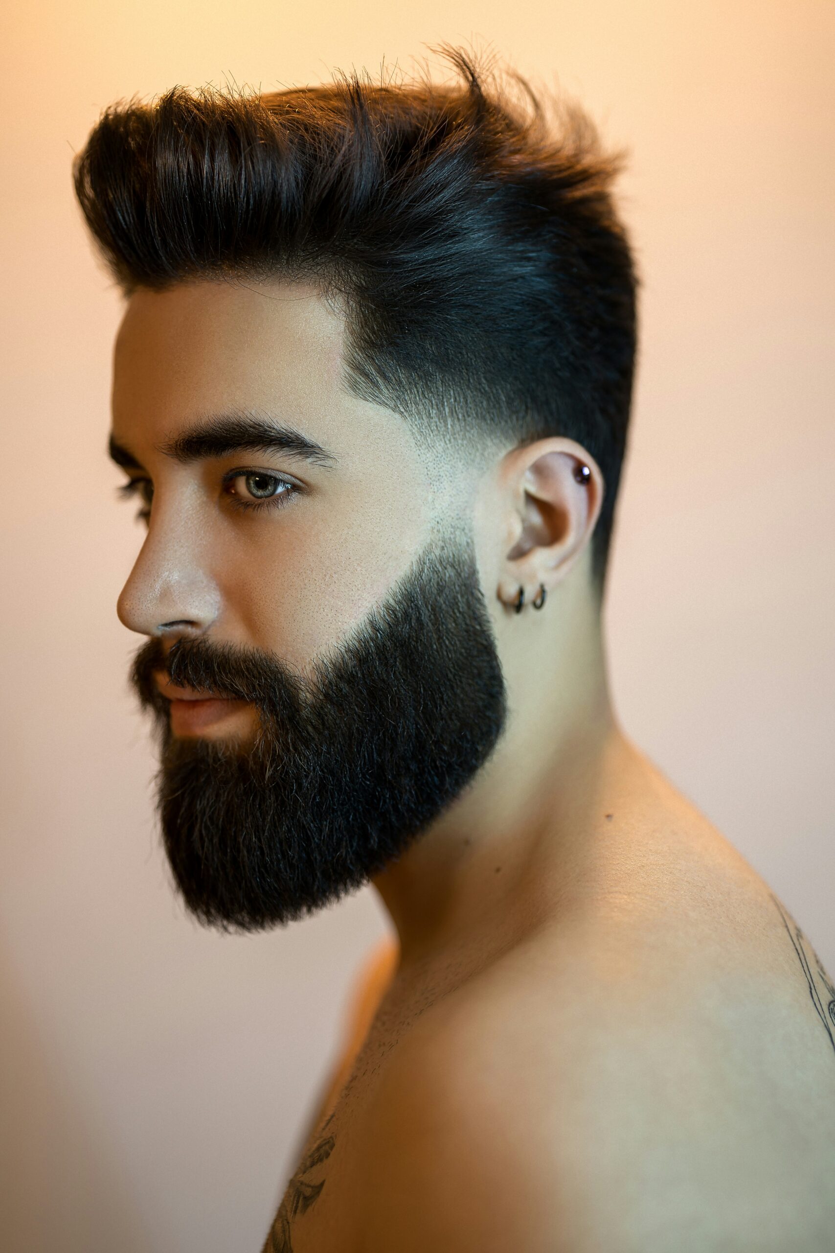 side profile image of smartly groomed young man with bare shoulders, sporting fashionable neatly styled slick hair and trimmed beard showing off hair colour for men dark brown black